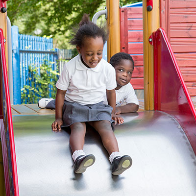 Ein kleines Mädchen bereitet sich darauf vor, eine Rutsche auf dem Spielplatz eines Kindergartens hinunterzurutschen.